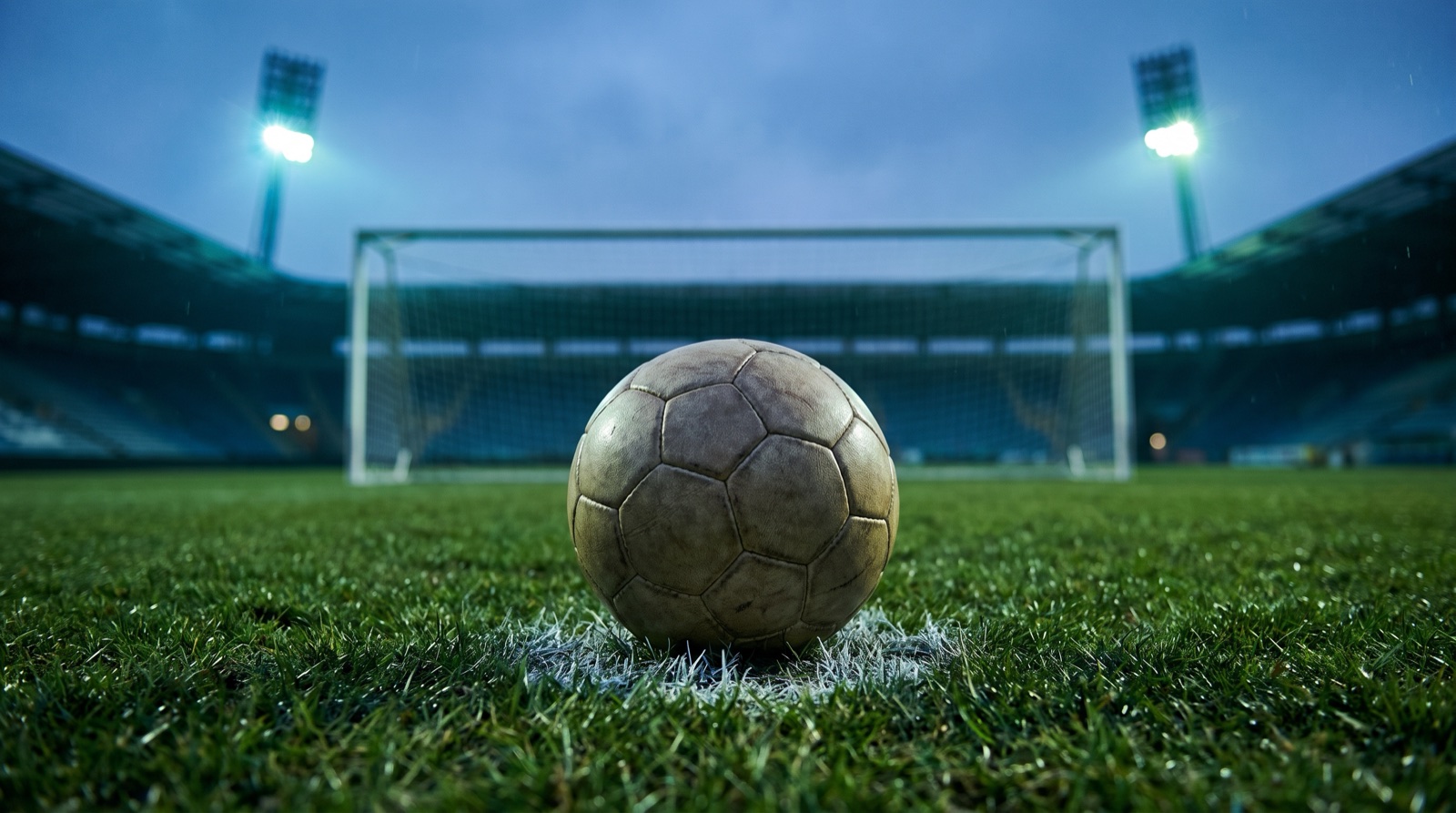 Balón de futbol en el punto penal con la portería y las luces del estadio desenfocadas al fondo