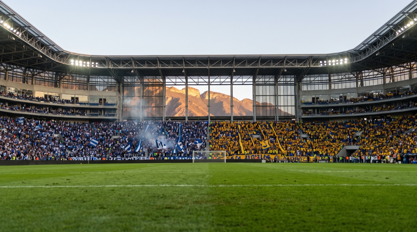Estadio de futbol lleno al atardecer en el norte de Mexico con aficion azul y amarilla antes del Clasico Regio