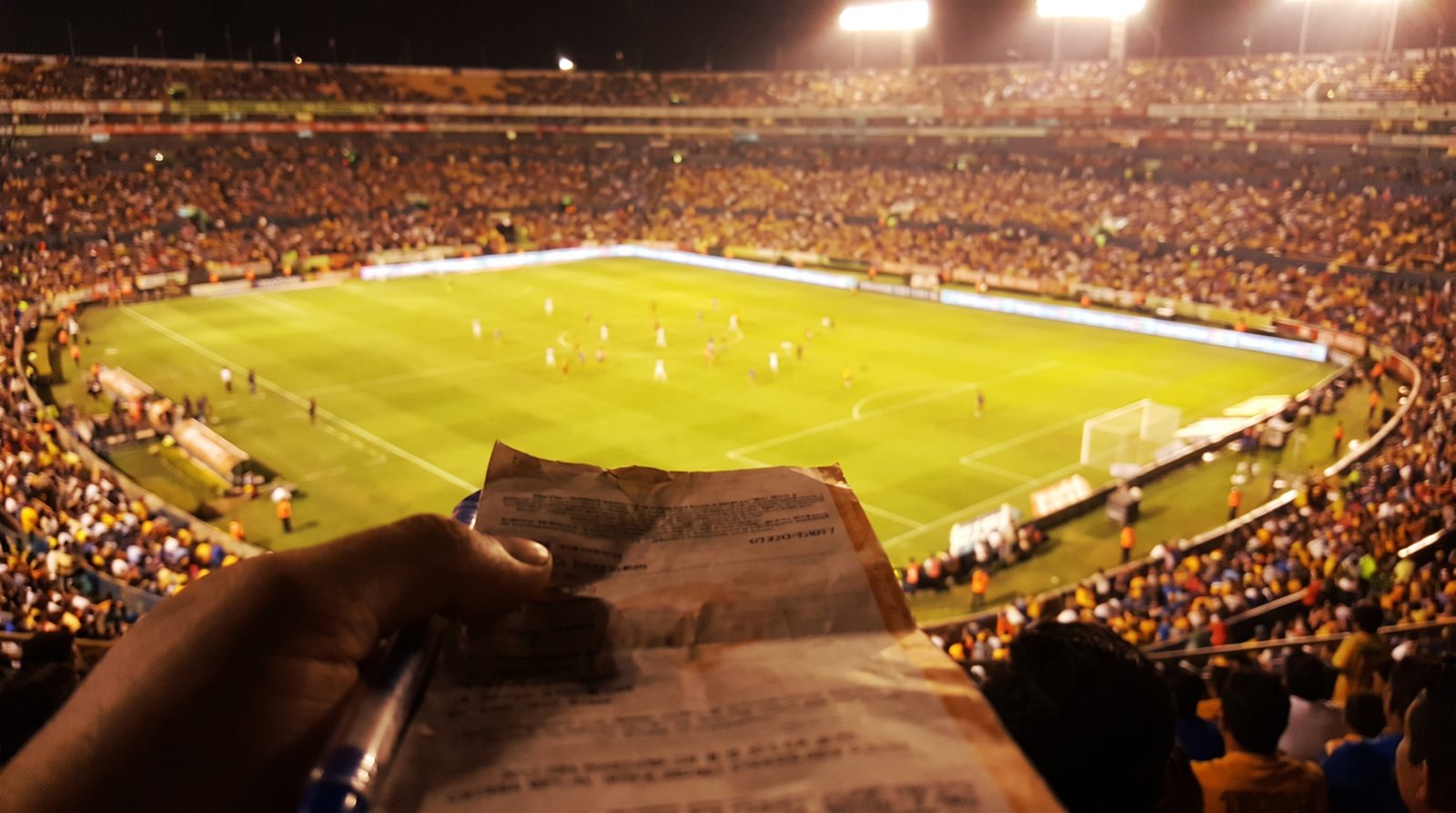 Aficionado con un boleto de quiniela en la mano durante un partido nocturno en un estadio lleno de México